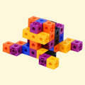 A set of colorful plastic building blocks arranged on a plain white background. The blocks come in multiple bright colors including orange, yellow, purple, blue, and black.